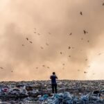 Mężczyzna stojący na wysypisku pełnym śmieci i dymu płonących odpadów