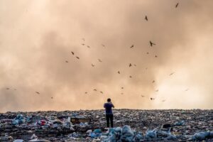 Mężczyzna stojący na wysypisku pełnym śmieci i dymu płonących odpadów