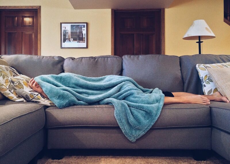 Śpiąca osoba na kanapie przykryta niebieskim kocem
