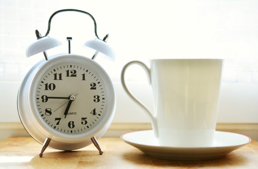 Tekst alternatywny (Alt Text): "Budzik ustawiony na godzinę siódmą obok białej filiżanki kawy.